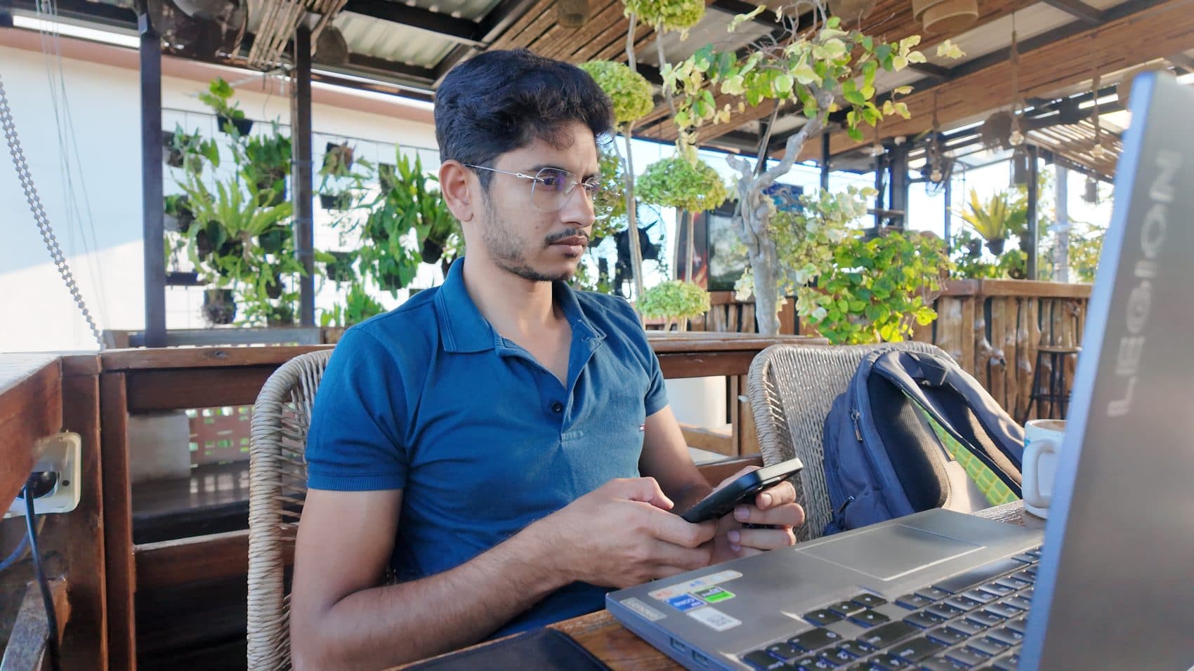Focused on a phone at a garden cafe in a blue polo